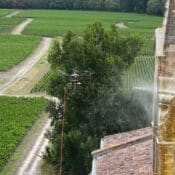 Drone professionnel effectuant le démoussage et le nettoyage d'un clocher d'église sans échafaudage.